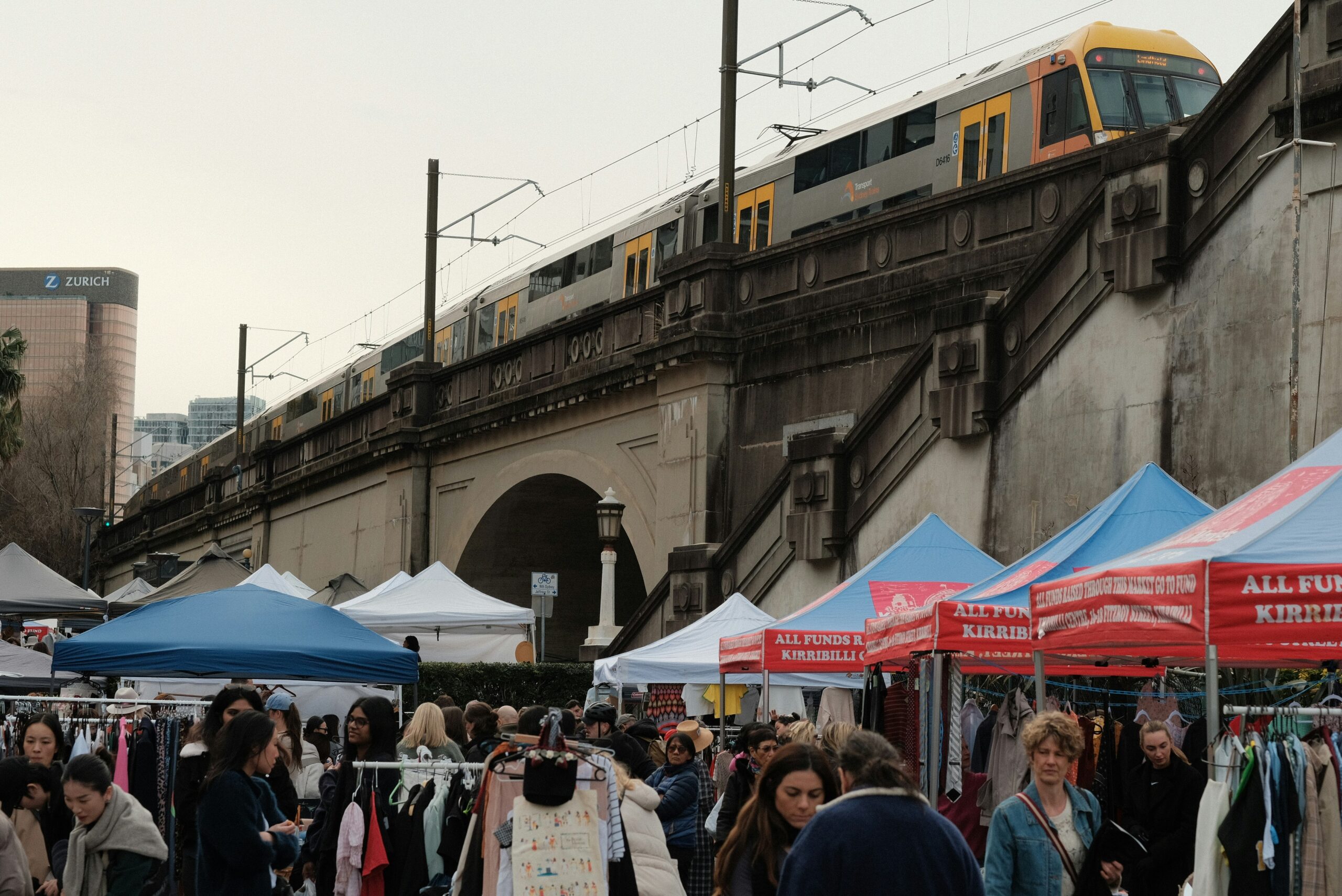 A crowd of people standing around tents with a train in the background