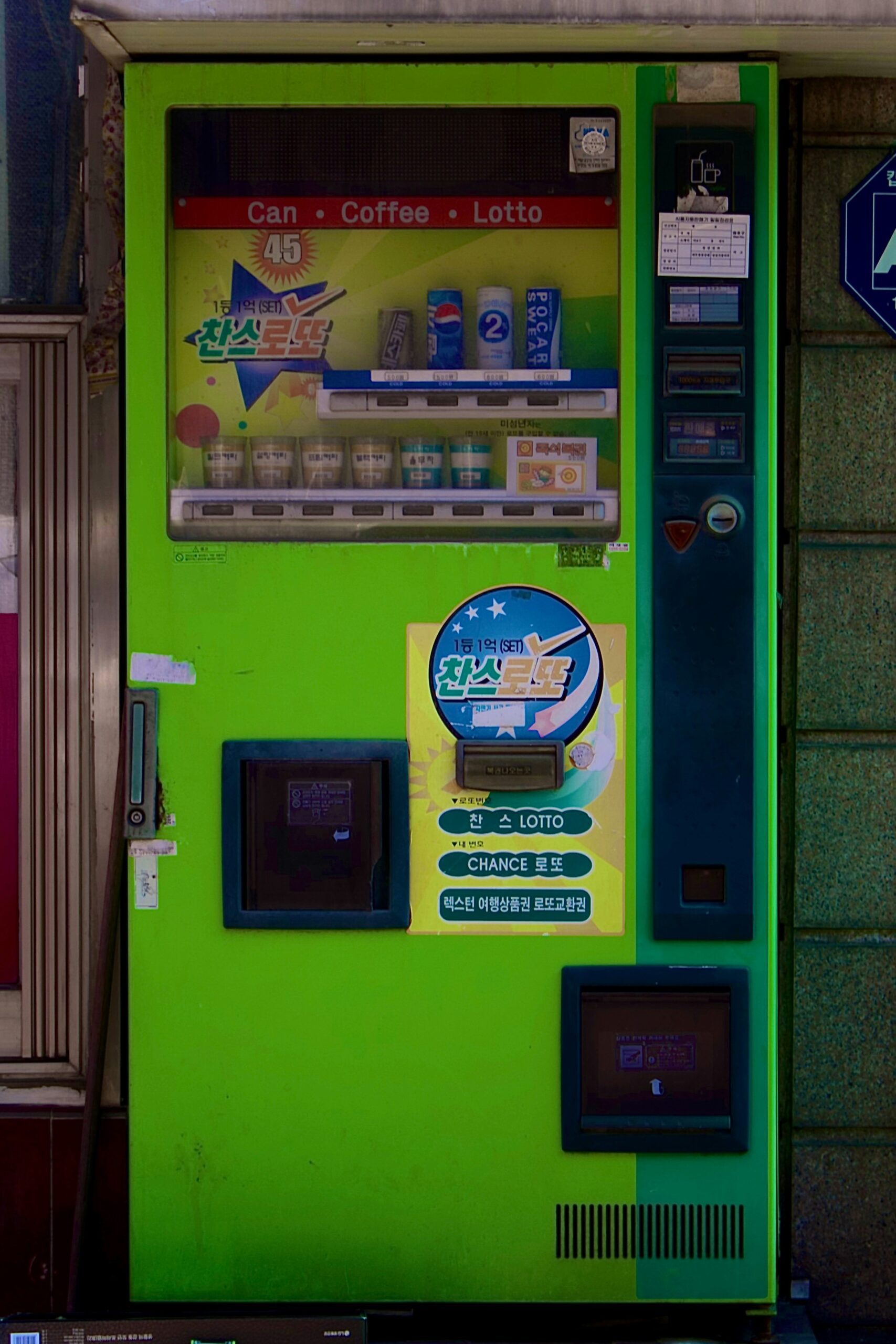 A green vending machine sitting next to a building