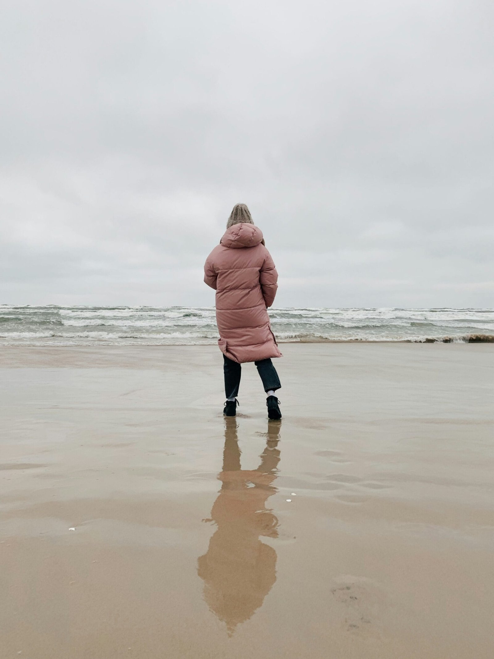 woman in pink hoodie standing on beach during daytime